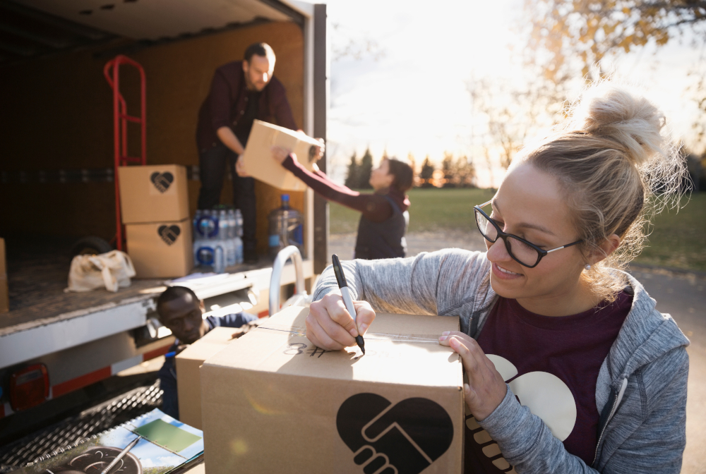 Female Volunteer Writing On Cardboard Box Outside Truck